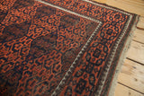 Antique Persian Belouch rug corner showing geometric madder red and navy gul motifs and original selvage.