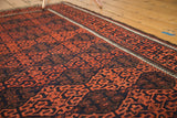 Detailed view of antique Belouch rug's madder red geometric gul motif and rich navy pile.