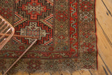 Intricate geometric patterns, vibrant red-orange tones, and worn edge on an antique Kurdish rug.