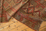 Close-up, folded antique Kurdish runner showing geometric patterns in red-orange, camel, brown with even wear and fringe.