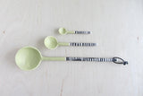 Large handmade sage green ceramic spoon with striped handle, shown with two smaller spoons.
