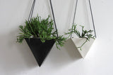 White porcelain triangle planter hanging with a green plant, beside a black planter.