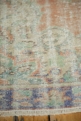 Distressed Oushak rug showing worn pile, blush, ivory, mint, and pale blue fringe.