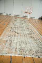 Distressed Oushak runner end with blush rose and charcoal patterns, visible knot heads, and ivory fringe.