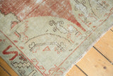 Distressed vintage Oushak rug corner detail showing wear to knot heads and a pomegranate red border.