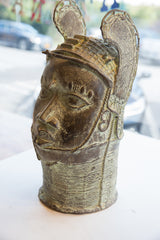 Side profile of a vintage Benin bronze head highlights its textured headdress and aged patina.
