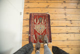 Overhead view of a small antique Serapi rug mat, showing its scale and asymmetric design on a floor.