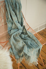 Handwoven denim indigo textile throw with fringed edges and soft, varied blue tones.