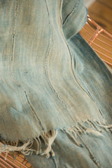 Collectible hand-woven denim indigo textile, showing faded blue hues, vertical seams, and frayed edges.