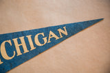 Vintage blue felt University of Michigan pennant showing gold 'IGAN' letters and pointed tip.