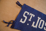 Close-up of blue felt St. Joseph's Villa pennant showing white 'St. Jos' text and ties.