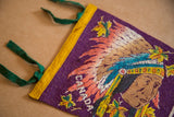 Detail: Native American figure's headdress with vibrant feathers and 'CANADA' on purple felt.
