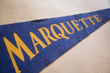 Close-up of vintage blue Marquette felt flag with gold QUETTE lettering, showing felt texture.