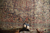 Antique Kermanshah rug's intricate scrolling florals in cochineal, navy, and camel, displaying mostly even wear.