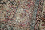 Worn cochineal red and blue floral motifs on an antique Kermanshah rug, revealing foundation.