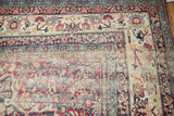 Antique Kermanshah carpet's faded floral design, showing extensive wear and a visible hole.