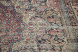 Kermanshah rug's scrolling floral design with cochineal, navy, and camel tones, showing mostly even wear.