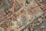 Worn Kermanshah rug detail, cochineal and pale blue scrolling floral motifs, low pile, near a metal leg.