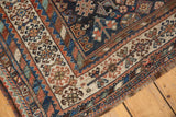Antique Kamseh rug corner with dark navy field, serrated plant motifs, and ivory-madder borders.