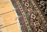 Close-up of antique Shirvan rug's finely woven geometric border in indigo, red, and beige with tattered fringe.