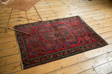 Vintage American Sarouk rug corner with dark floral border, cherry red field, and tattered fringe.