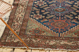 Hamadan rug runner corner showing indigo Herati design, geometric borders, and tattered fringe.