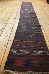 A long perspective view showing the repeating geometric panels of an antique Belouch soumac runner.