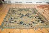 Antique Caucasian rug corner with sand field, dark navy geometric patterns, and tattered fringe.