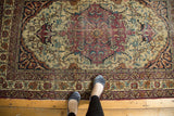 Ornate central medallion, sprawling vinery on antique Kermanshah rug with cochineal red, ivory, blue, visible foundation.