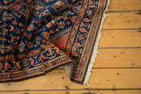 Folded vintage Engelas rug showing indigo blue Herati pattern, terra cotta border, and fringe edge.
