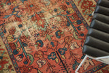 Detail of worn rectilinear floral motifs on a faded red and blue antique Malayer rug.