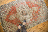 Distressed Oushak rug's central geometric medallion, dusty red field, and exposed foundation.