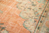 Textured peach and ivory distressed Oushak rug showing mint green floral motifs and worn areas.