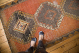 Distressed Oushak runner, geometric charcoal and bronze diamond medallions on faded orange.
