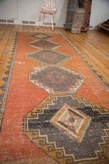 Distressed Oushak runner with dusty bronze copper field, charcoal diamond medallions, and worn pile.