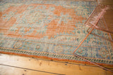 Distressed Oushak rug texture showing faded tangerine orange, royal blue, and ivory motifs.