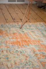 Angled view of vintage distressed Oushak rug with faded tangerine, blue, and ivory colors.