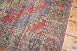 Distressed Oushak rug corner showing geometric spandrels, faded red, blue, and ivory tones.