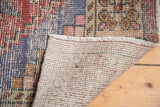Distressed Oushak runner pile with red and blue pattern, revealing hand-knotted foundation and fringe.
