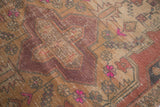 Geometric motif detail of a distressed Oushak rug with worn texture and pink accents.