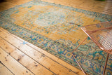 Distressed gold Oushak carpet with brilliant royal blue and mint green floral patterns.