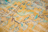 Distressed Oushak rug pile with bright gold, mint green, and blue floral motifs.