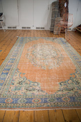 Distressed Oushak carpet with worn peach apricot field, faded royal blue, and mint floral borders.