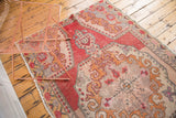 Vintage distressed Oushak rug with prominent abrash, beige field, and pomegranate red rococo border.