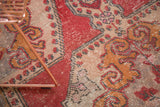 Textural close-up of distressed Oushak rug with abrash, worn pile, and red-gold rococo motifs.