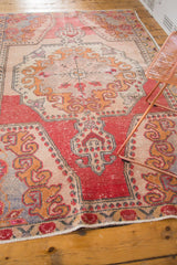 Pomegranate red border, beige field, and bright gold rococo motifs on the distressed Oushak rug.