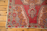 Distressed vintage Oushak rug corner showing red, gold, beige, and pink plant motifs.