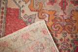 Distressed Oushak rug corner showing worn red, gold pile and hand-knotted beige foundation.