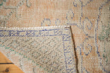 Distressed vintage Oushak rug with low peach pile, visible foundation, and secured edge.