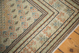 Distressed Oushak rug corner: muted green border, charcoal lines, mini boteh motifs.